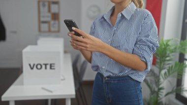 Beyaz kadın kapalı seçim merkezindeki oy verme kabininin yanında akıllı telefon kullanıyor.