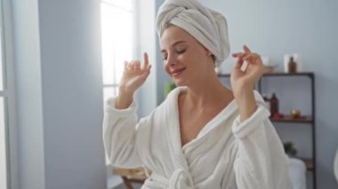 Huzurlu bir spa odasında kafasında bornoz ve havlu olan bir kadın, rafları ve pencereleri olan bir sağlık merkezinde dinleniyor.