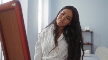 Spa odasında dinlenmekten hoşlanan bir kadın, beyaz bir bornoz giyiyor, uzun kumral saçları şelale gibi aşağı iniyor, penceresinden içeri ışık süzülen sakin bir arka plan.