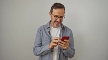 İspanyol orta yaşlı bir adam akıllı telefon kullanıyor ve izole edilmiş beyaz arka planda mutlu bir gülümseme ve olumlu onay işareti gösteriyor.