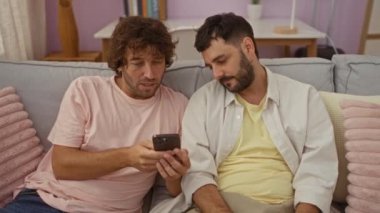 Oturma odasındaki bir kanepede oturan erkekler, akıllı telefona bakıyorlar ve iletişim ve tartışma anlarını paylaşıyorlar..