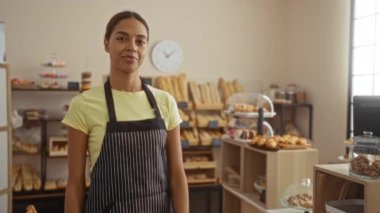 Sıcak bir kafede fırın ürünleri sunan bir kadın. Ahşap raflarda taze pişmiş ekmek ve hamur işleri sergileniyor.