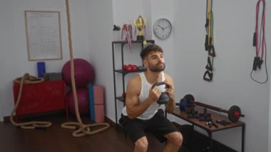 Spor salonunda kettlebell kaldıran genç İspanyol adam halat ve dambıl gibi ekipmanlarla yoğun bir idman yapıyor.