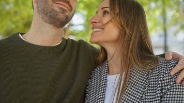 Mutlu bir kadın açık havada gülümseyen bir adamı kucaklıyor, sevgi dolu bir ilişki tasvir ediyor..