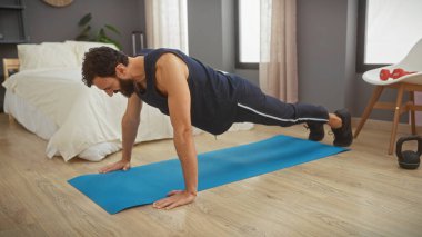 Modern bir yatak odasında mavi bir paspasın üzerinde şınav çeken kaslı bir adam. Spor salonu ve evde sağlıklı bir yaşam tarzı..