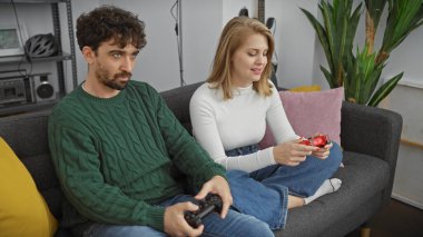 Bir erkek ve bir kadın evdeki boş zamanlarını gösteren rahat bir oturma odasında video oyunları oynuyorlar..