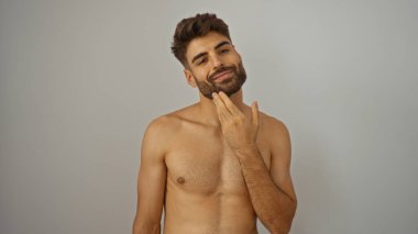 Genç, çekici, sakallı İspanyol bir adam izole edilmiş beyaz bir arka planda kendini tımar ediyor..