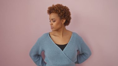 Pembe arka planda poz veren mavi kazaklı Afro-Amerikalı bir kadın.