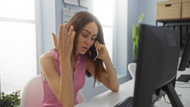 Telefonda konuşan genç bir kadın ofiste hayal kırıklığına uğramış bir halde bilgisayarın yanına kuruluyor.