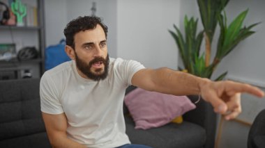 Modern bir oturma odasını işaret eden sakallı adam aciliyet ve istikameti ifade eder, gelişigüzel bir ortamda etkileşimi ima eder..