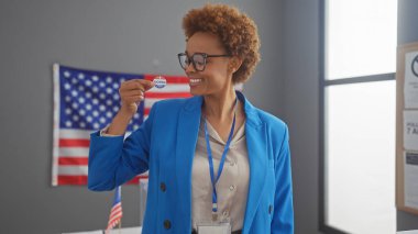 Mavi ceketli Afro-Amerikalı bir kadın kapalı bir alanda Amerikan bayrağıyla 'oylanmış' bir çıkartma sergiliyor.