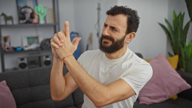 Sakallı adam silah jesti yapıyor, modern dekor ve oturma odası arka planında bitkiler..