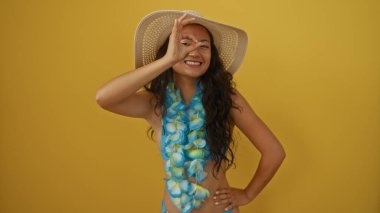 Genç Çinli kadın, sarı arka planda mavi bir lei ve hasır şapka giyerken gözlerinin önünde güzel bir jest yapıyor.