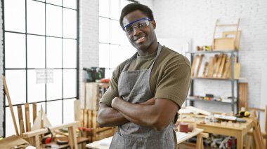 İyi donanımlı bir atölyede kollarını kavuşturmuş kendinden emin Afro-Amerikan erkek marangoz.