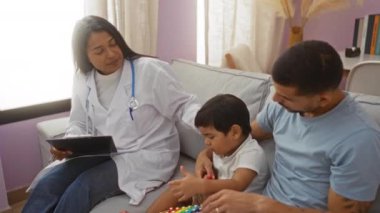 Çocuk doktoru, baba ve oğlunu evinde ziyaret edip çocuk sağlığını tartışıyor ve rahat oturma odasında ksilofon çalıyor.