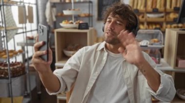 Genç bir adam pastanede video görüşmesi yapıyor, kulaklık takıyor ve elinde fırın malzemeleri olan bir telefon tutuyor.