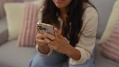 Rahat bir oturma odasında rahat bir koltukta otururken akıllı telefon kullanan bir kadın modern teknolojiyi ve rahat ev ortamını sergiliyor..