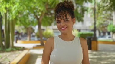 Güneşli bir günde, yemyeşil arka planda, şehir parkında gülümseyen genç bir kadın.