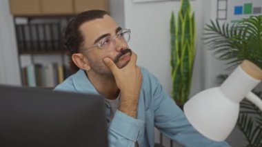 Ofiste bıyıklı yakışıklı bir adam. Derin düşüncelere dalmış. Masasında mavi gözlüklü, bitkilerle çevrili bir adam.