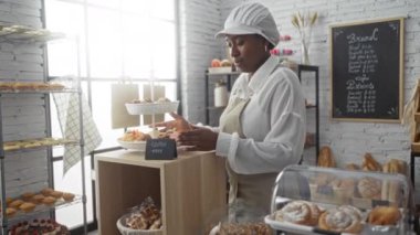 Bir pastanede çalışan genç bir kadın, arkasında fırınlanmış mallarla birlikte kapalı bir ortamda lezzetli hamur işleri organize ediyor.