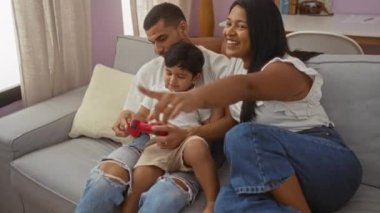 Aile kanepede video oyunu oynuyor. Kadın ve erkek, rahat oturma odasında çocuğa yardım ediyor.