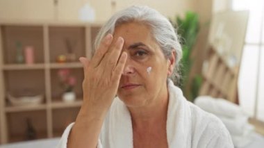 Yüzüne krem sürmüş beyaz bir bornoz giyen yaşlı bir kadın huzur veren bir güzellik merkezine başvurmuş.