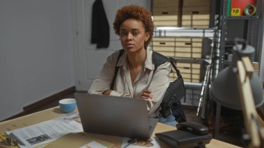 Ofis masasında dizüstü bilgisayarla çalışan odaklanmış Afro-Amerikan kadın dedektif..