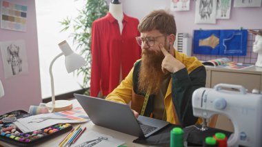 Kızıl sakallı adam, renkli bir terzi dükkanında manken ve dikiş makinesi tasarlarken kafa yorar.