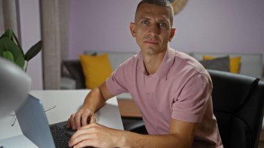 Evinin rahat oturma odasında dizüstü bilgisayarda çalışan yakışıklı genç adam.