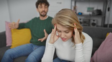 Sıkıntılı bir kadın, arka planda bulanık bir şekilde el kol hareketi yapan bir adam, modern oturma odasındaki çatışmaları gösteriyor..