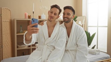 Erkekler spa odasında selfie çekiyorlar, beyaz bornozlar giyiyorlar ve gülümsüyorlar, sağlık merkezinde sevgi ve rahatlama gösteriyorlar..