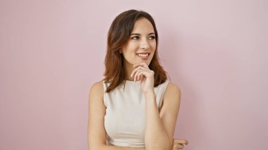 Çekici bir saç stili olan düşünceli, genç bir İspanyol kadın pembe izole bir duvara poz veriyor..