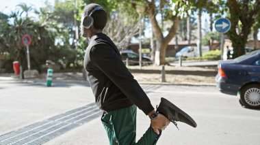 Kulaklık takan Afro-Amerikalı genç adam bulanık bir geçmişi olan güneşli bir şehir sokağından geçiyor..