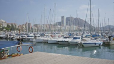 Açık deniz tekneleri ve berrak mavi gökyüzünün altında bir şehir manzarası olan açık deniz marinasının bulanık arkaplanı, su ve uzak dağların dağılmış manzarasına ev sahipliği yapıyor..