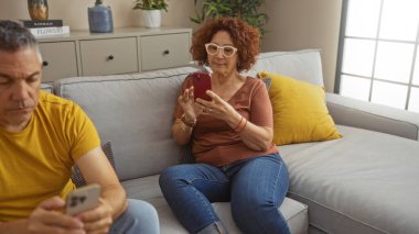 Modern dairenin oturma odasında akıllı telefon kullanan orta yaşlı bir çift..