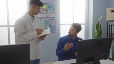İki adam, bir ofiste çalışıyor, iyi aydınlatılmış bir odada notlar ve diyagramlarla dolu bir tahtayla tartışıyor ve notlar alıyorlar.