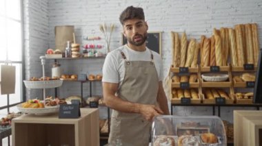 Genç adam fırında çalışıyor. Taze ekmek ve hamur işleriyle çevrili.