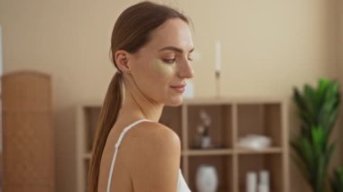 Spa Sağlık Merkezi 'nde genç ve güzel bir kadın cilt bakımı için göz altı bantları takıyor. Kapalı alanda rahat bir arka plana gülümsüyor..