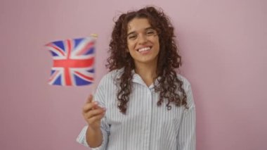 İngiliz bayrağı tutan genç bir kadın pembe arka planda gülümsüyor.