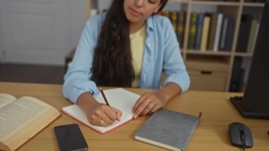 Genç, güzel, Latin bir kadın kitap ve ciltlerle dolu bir çalışma odasında yazıyor.