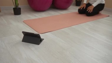 Spor salonundaki pembe minderde yoga yapan kadın tabletle yerde.