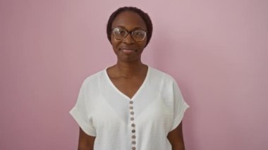 Gözlüklü ve tişörtlü Afro-Amerikalı genç bir kadın. El yazısı, gülümseme ve başarı işareti gösteriyor. Tecrit edilmiş pembe arka planda.