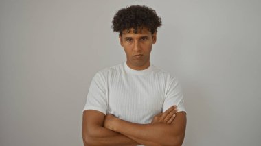 Beyaz tişörtlü, kolları çapraz beyaz arka planda duran İspanyol genç adam.
