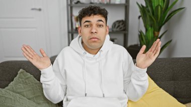 Belirsiz bir genç adam rahat bir evde, rahat bir kapüşonlu giyerek omuz silkiyor.