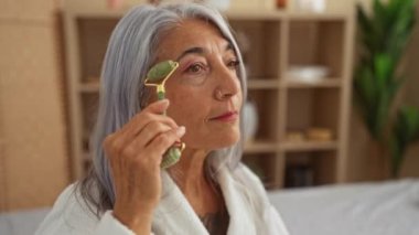 Gri saçlı yaşlı bir kadın spa odasında yeşil bir silindir kullanıyor. Huzurlu bir güzellik ve sağIık ortamı yaratıyor..