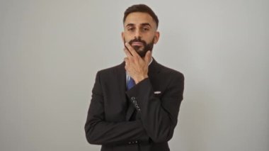 Takım elbiseli genç İspanyol adam özgüvenle beyaz arka planda poz veriyor düşünceli bir ifadeyle.