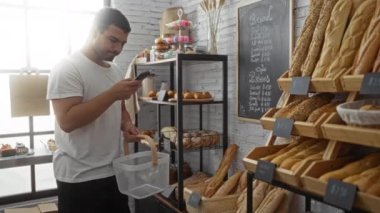 Genç adam telefonda fırının içinde bir sepetle konuşuyor. Kapalı bir dükkanda çeşitli ekmek ve hamur işleri sergiliyor.