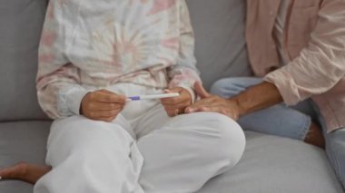 Evdeki koltukta oturan çift, elinde hamilelik testi olan bir kadın ve dokunuşla rahatlayan bir erkek, kapalı bir ortamda ilişki ve samimiyeti simgeliyor.