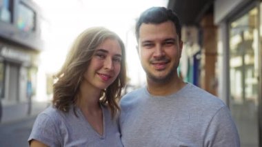 Aynı gri tişörtleri giyen gülümseyen çift güneşli bir şehir sokağında birlikte vakit geçiriyorlar. Canlı bir şehir ortamında birbirlerine olan sevgilerini vurguluyorlar.