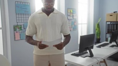 Çevresinde düzenli panolar ve bilgisayar istasyonları olan parlak bir ofis ortamında gazete okuyan genç adam verimli bir çalışma alanı öneriyor.